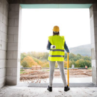 Female worker on the building site. Young woman holding blueprints. House construction. Rear view.