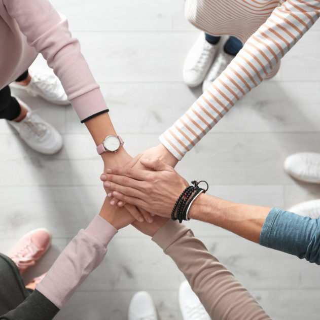 People holding hands together over light wooden background, top view. Unity concept